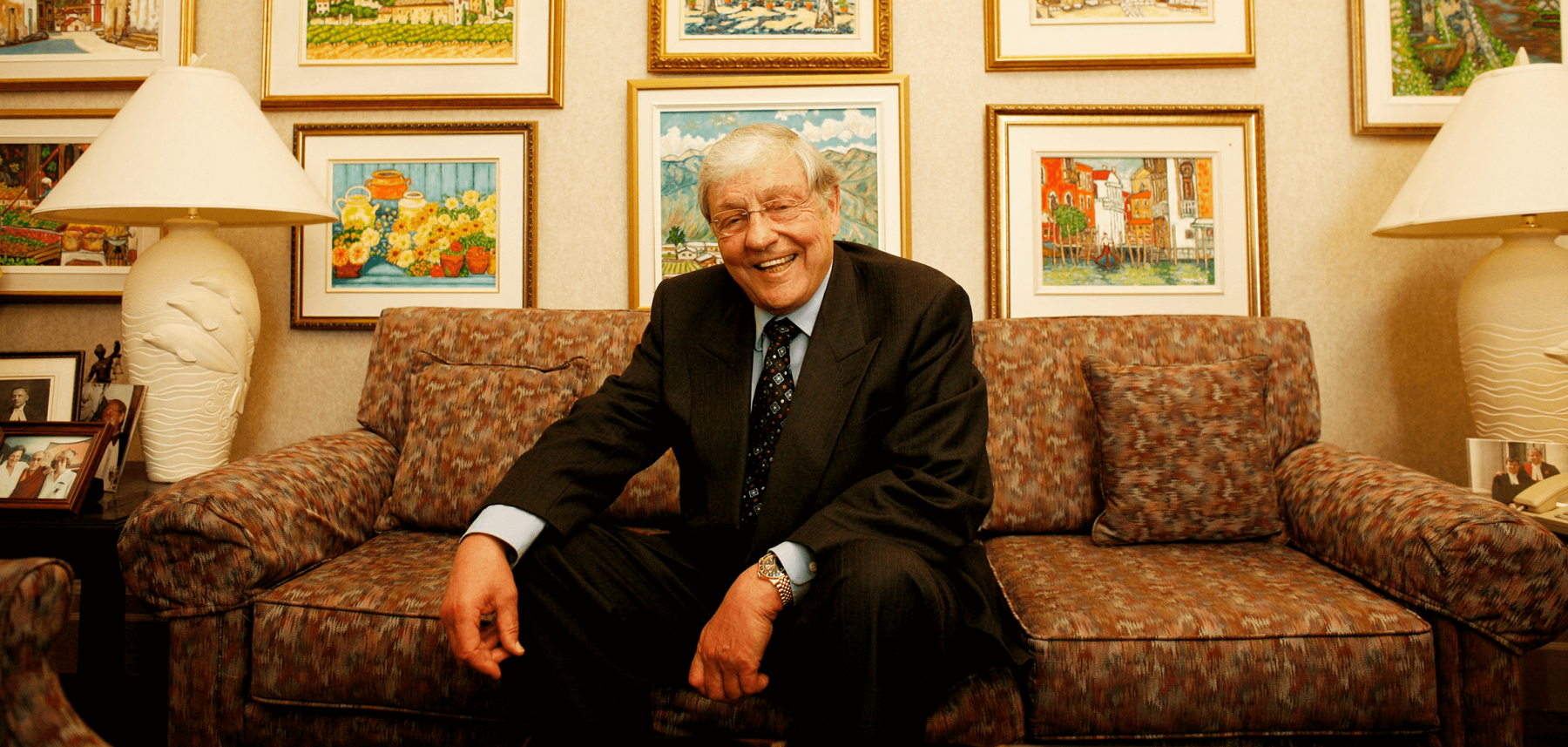 Photo of The Honourable R. Roy McMurtry in front of his many paintings